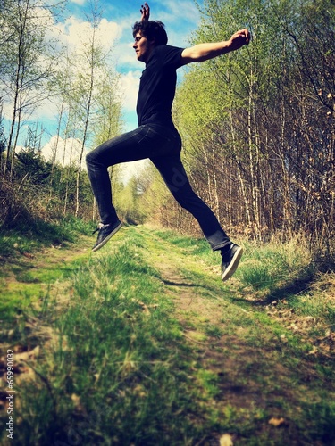young man jumping over forest path