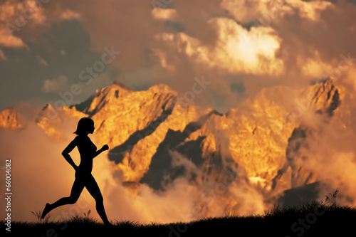 Silhouette of a woman running jogging in the mountains at sunset