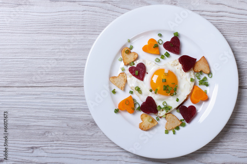 Fried potatoes, carrots, beets and egg of heart on a plate.