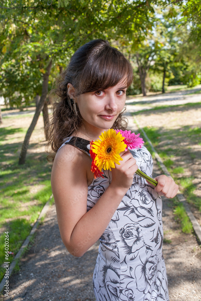Fototapeta premium Brunette women in city park with flowers in her hands