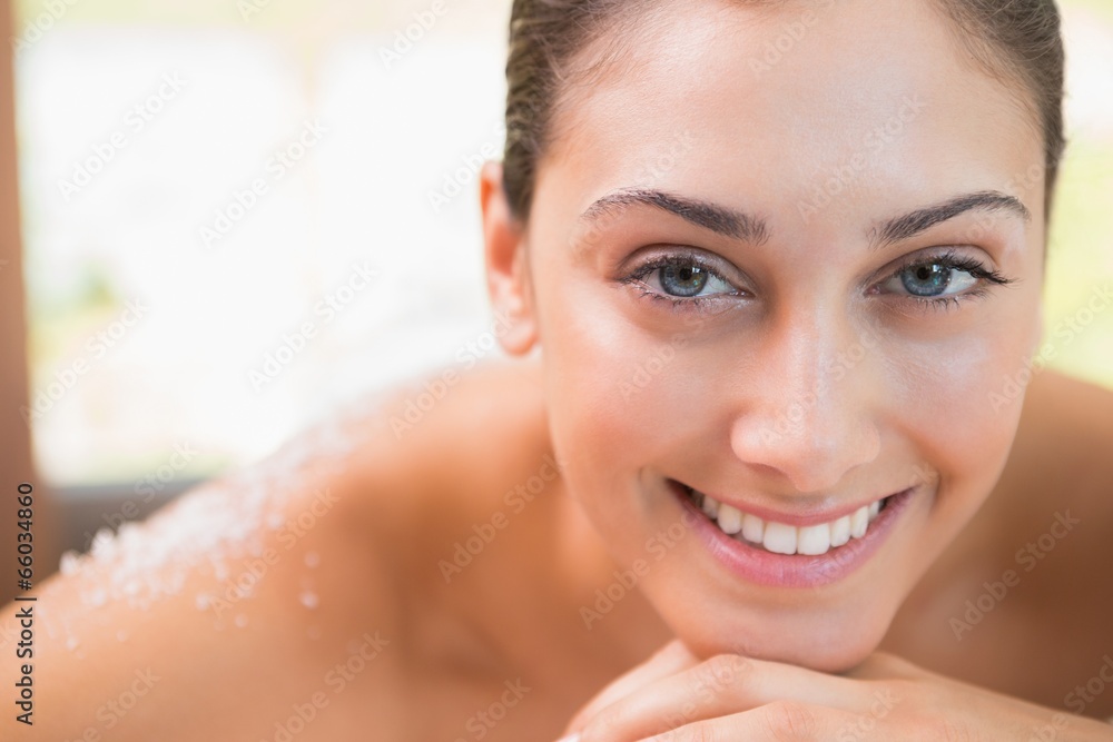 Beautiful smiling brunette lying on massage table with salt scru Beautiful smiling brunette lying on massage table with salt scru