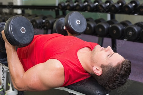 Bodybuilder lying on bench lifting heavy dumbbells