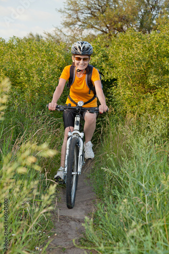 Happy adult woman riding bicycle from the dense bush