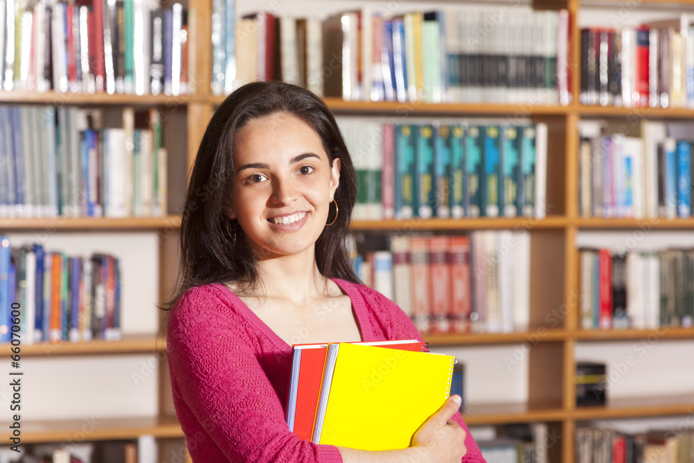 Happy female student holding books at the library Happy female student holding books at the library