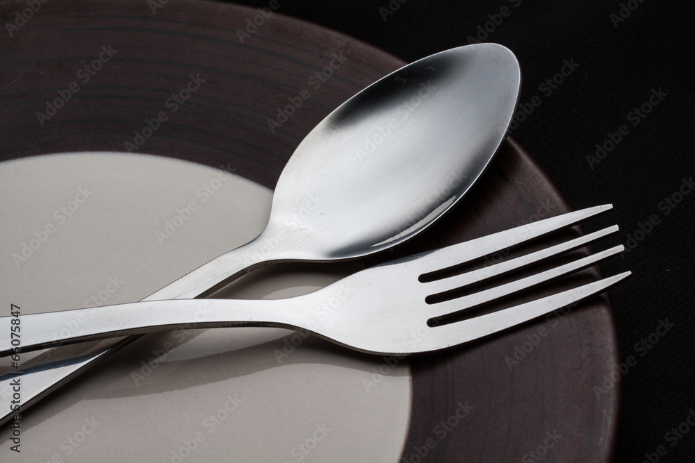 Plates with a silver fork and spoon isolated on black backgroun Plates with a silver fork and spoon isolated on black backgroun