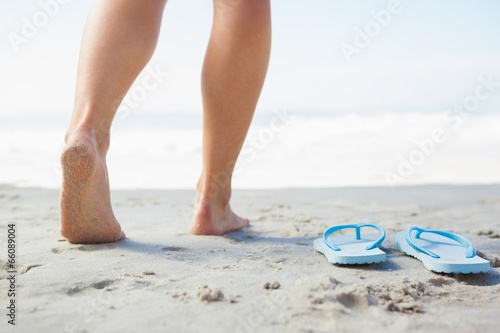 Female feet stepping on sand beside flip flops