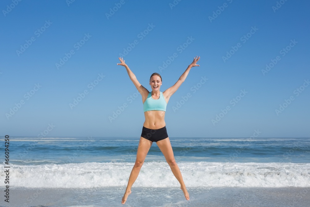 Fit woman jumping on the beach with arms out Fit woman jumping on the beach with arms out