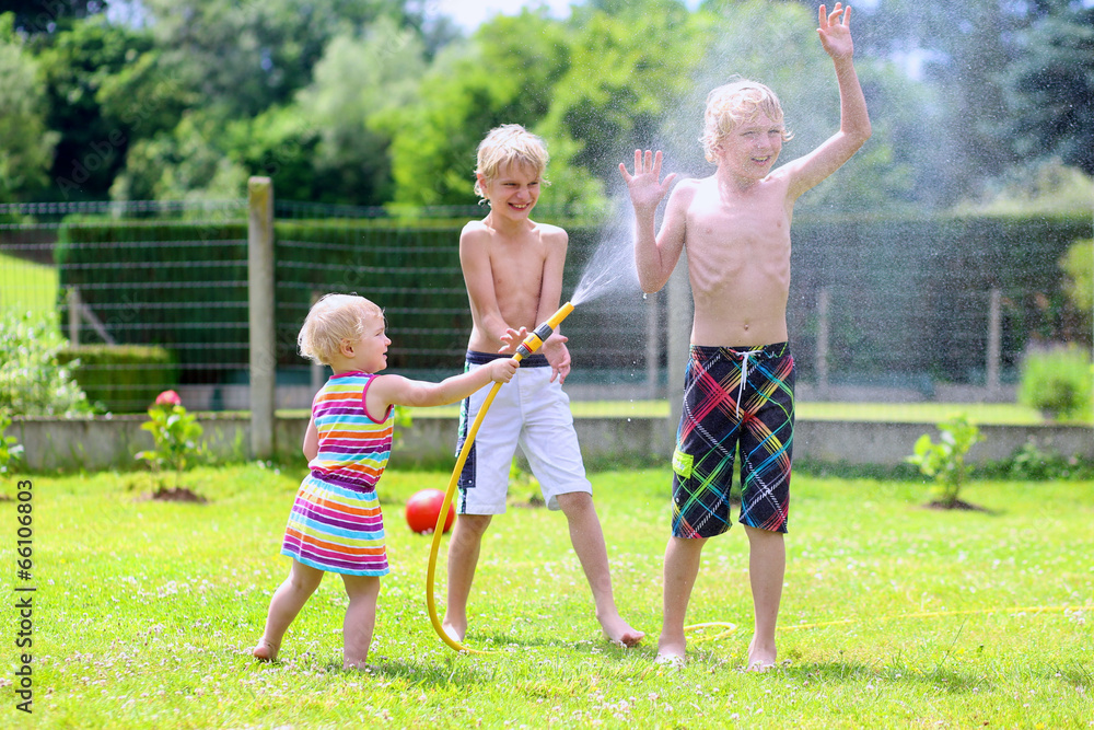 Fototapeta premium Happy siblings kids playing in the garden with watering hose