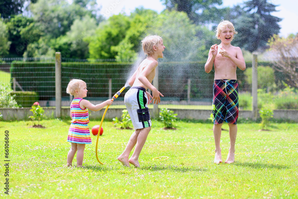 Happy siblings kids playing in the garden with watering hose