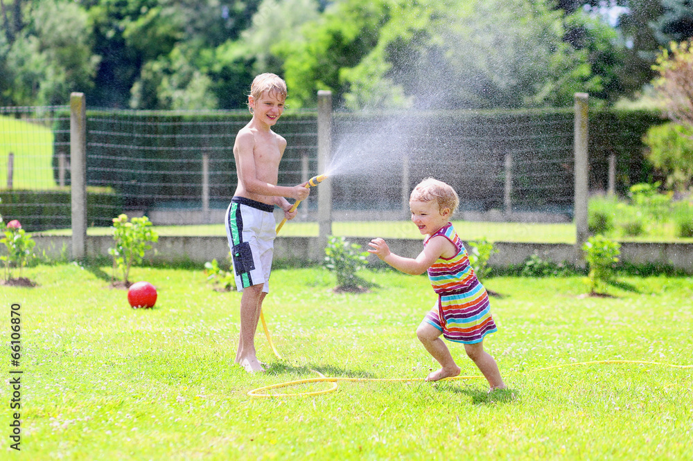 Brother and sister playing in the garden with watering hose