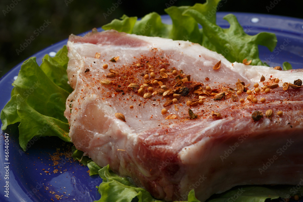 Raw pork steak sprinkled with pepper on blue plate with salad