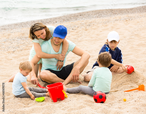 Happy parents and kids toying with sand