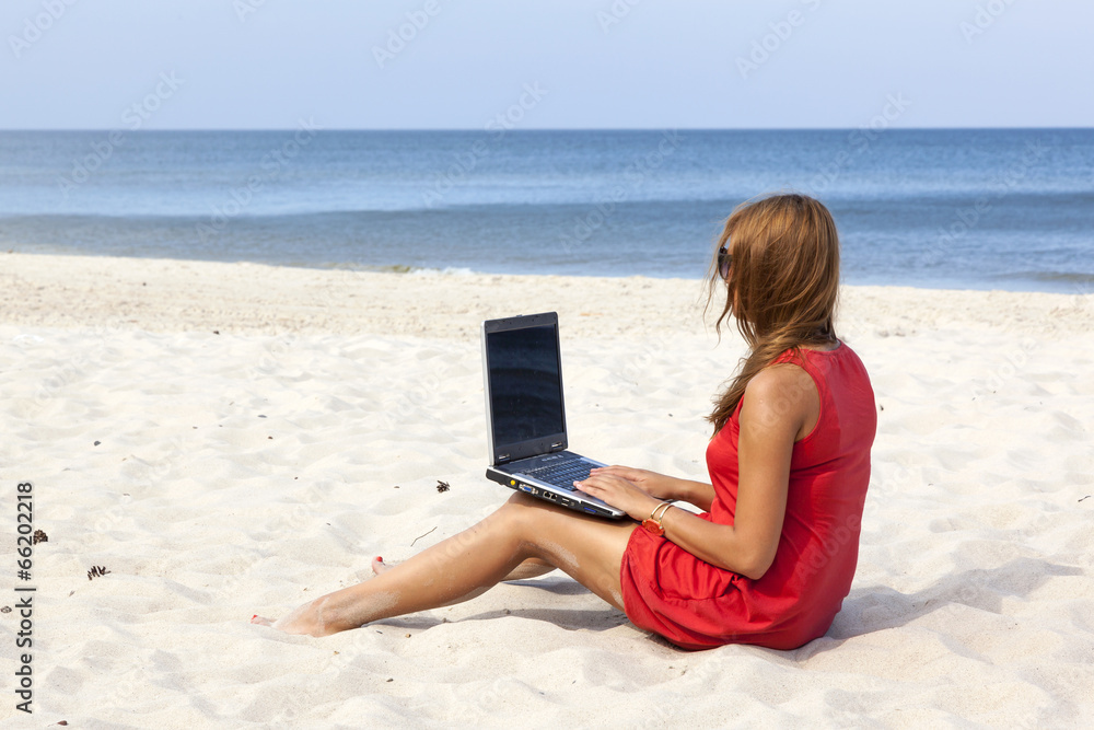 Woman is sitting with laptop on the beach.