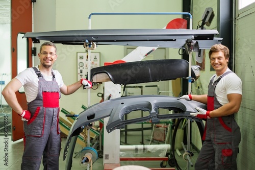 Two workers with car bodykit ready for painting in a workshop photo