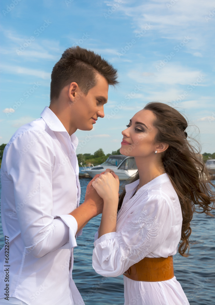 Guy holding hands a girl on a wooden pier near the water.