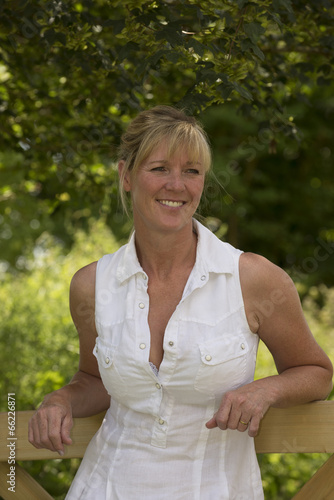 Konstfotografi Portrait of a woman in a summer dress leaning on a fence