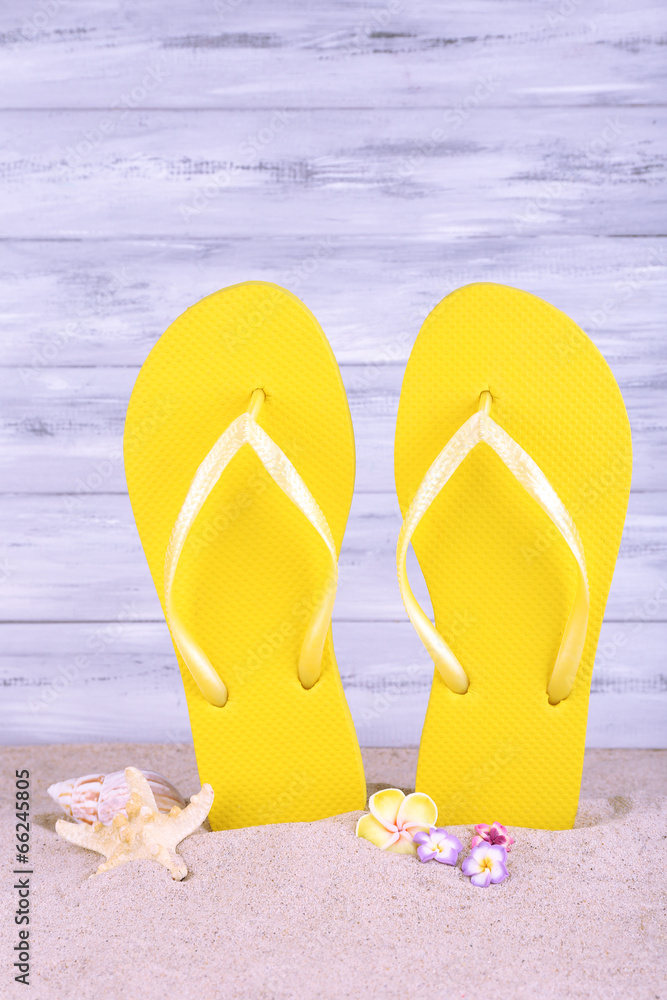 Fototapeta premium Bright flip-flops on sand, on wooden background