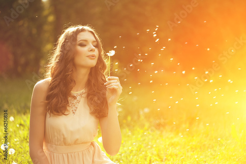 Beautiful young woman blowing a dandelion. Trendy young girl at