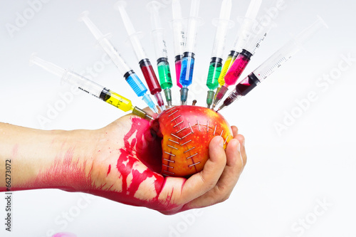 hand holding gmo apple surrounded by syringe with blood photo