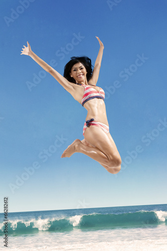 Joyful woman in bikini jumping on beach