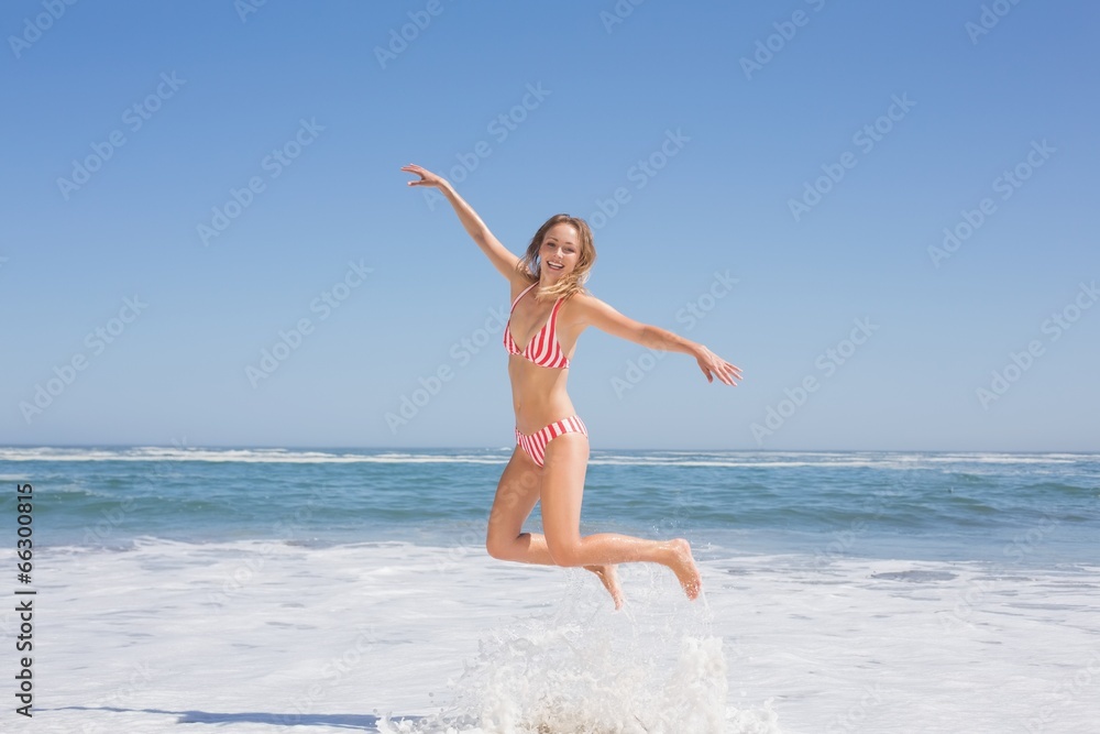 Happy fit woman in bikini jumping on the beach