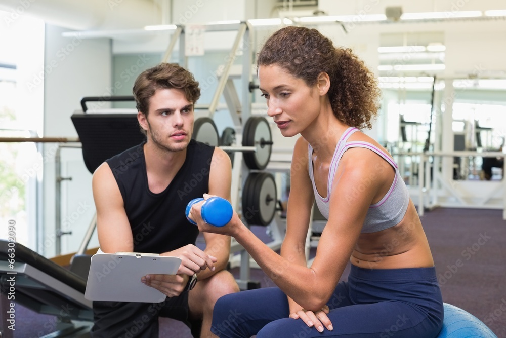 Obraz premium Trainer watching client lift dumbbells on exercise ball