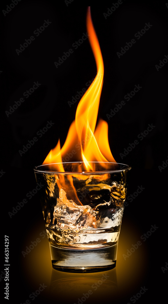 Glass with whiskey splash and fire on black background