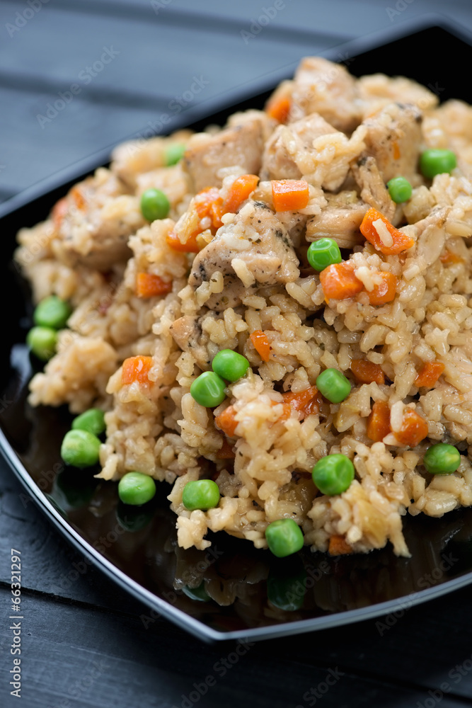 Pilaf with chicken, green peas and carrot in a black plate Pilaf with chicken, green peas and carrot in a black plate