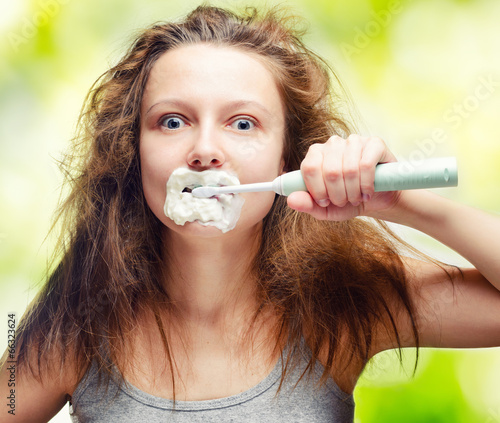 Shaggy young woman using electric toothbrush photo