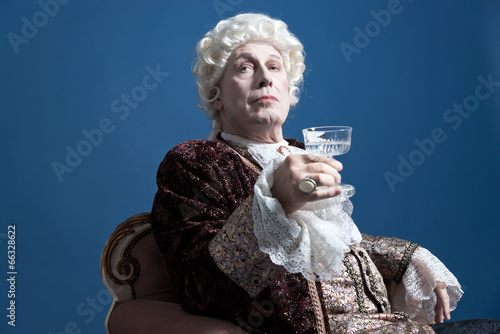 Retro baroque man with white wig holding a wine glass sitting on photo