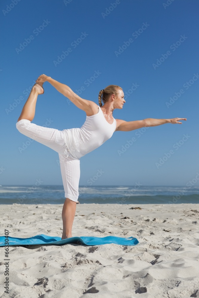 Blonde woman standing in warrior pose on beach