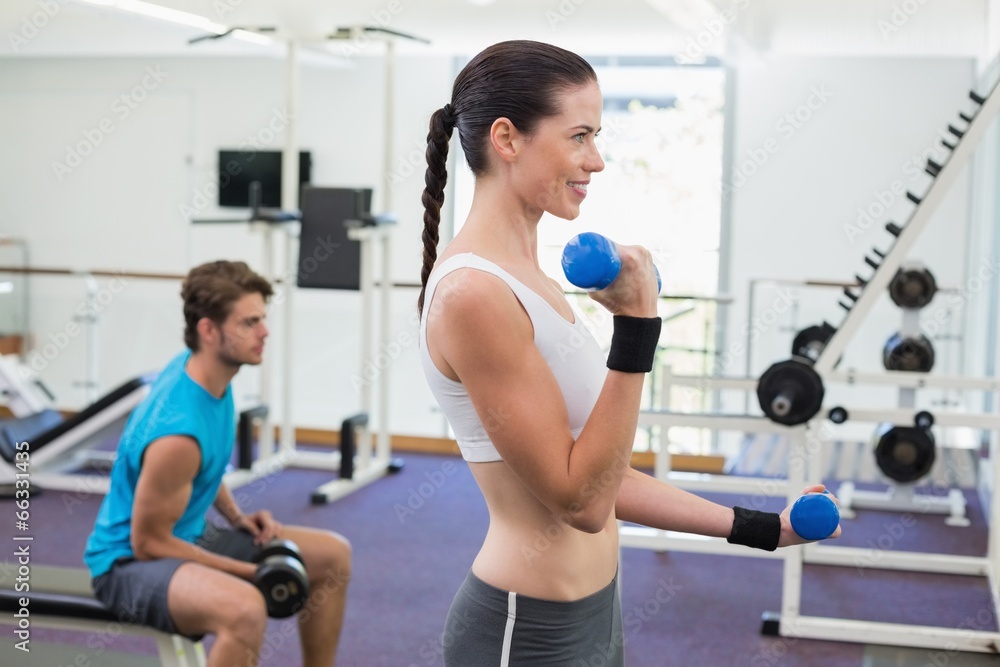 Fit brunette exercising with blue dumbbells Fit brunette exercising with blue dumbbells