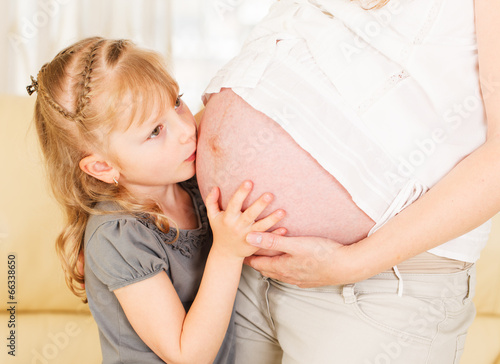 Valokuva Girl kissing her mother's pregnant belly.