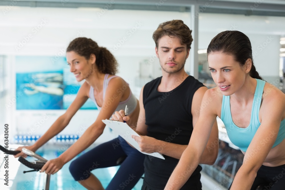 Fit women in a spin class with trainer taking notes Fit women in a spin class with trainer taking notes