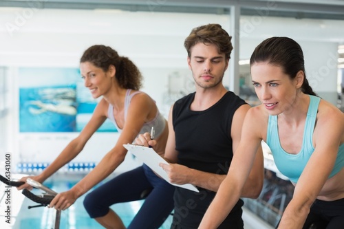 Fit women in a spin class with trainer taking notes © WavebreakmediaMicro