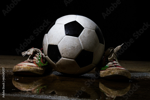 Dirty sneakers with soccer ball on black background