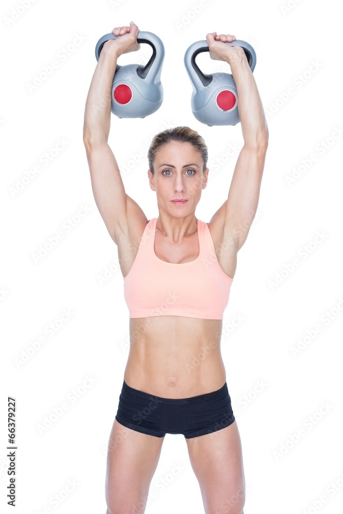 Serious female crossfitter lifting kettlebells above head Serious female crossfitter lifting kettlebells above head
