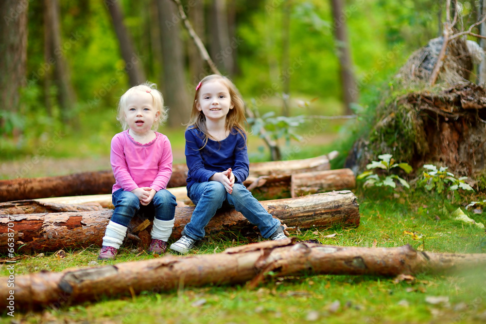 Two little sisters sitting on a log in a forest Two little sisters sitting on a log in a forest