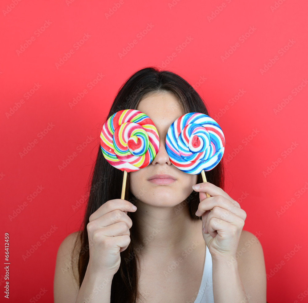 Portrait of woman covering eyes with lollipops against red backg