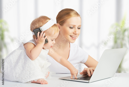 mother with baby daughter works with a computer and phone