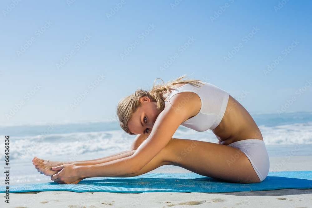 Gorgeous fit blonde in seated forward bend pose on the beach Gorgeous fit blonde in seated forward bend pose on the beach