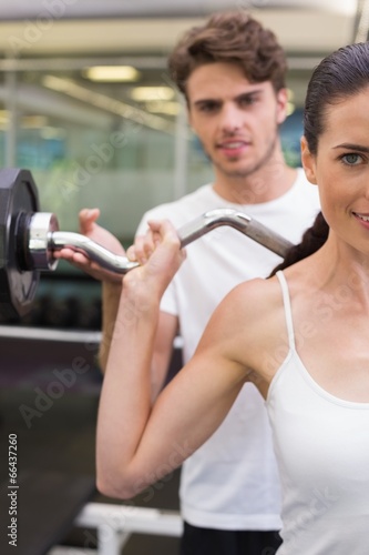 Fit smiling woman lifting barbell with her trainer