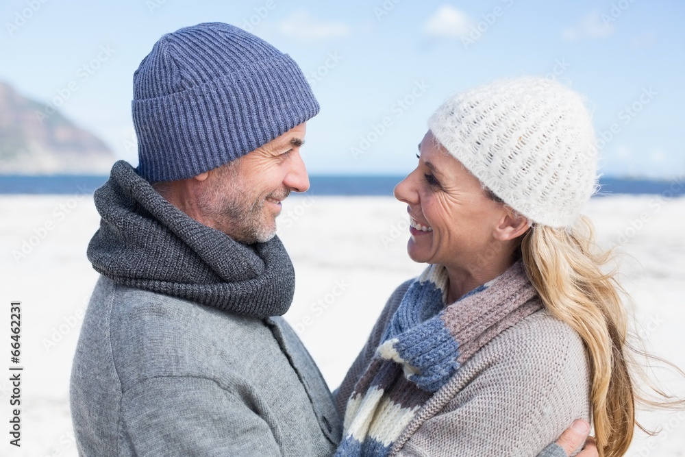 Attractive couple smiling at each other on the beach in warm clo Attractive couple smiling at each other on the beach in warm clo