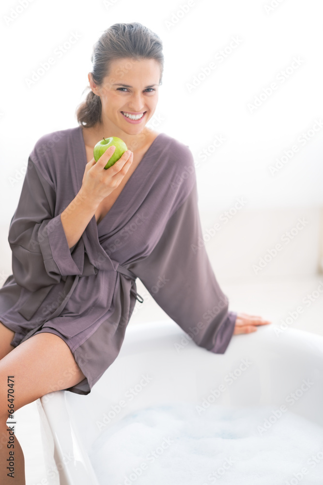 Happy young woman with apple sitting on bathtub Happy young woman with apple sitting on bathtub