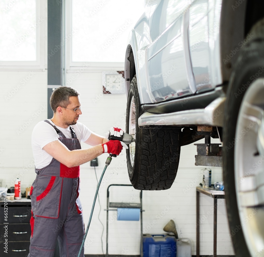 Serviceman unscrewing wheel in car workshop Serviceman unscrewing wheel in car workshop