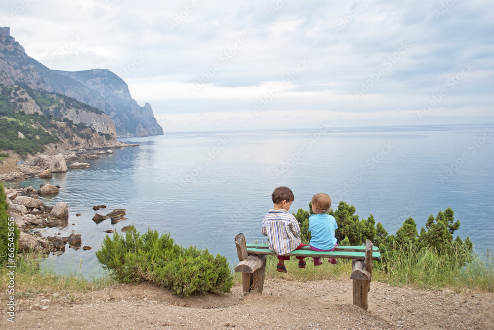 Children on a bench on the seafront overlooking the rocks, ocean