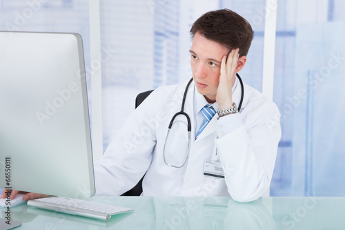 Worried Male Doctor Using Computer At Desk