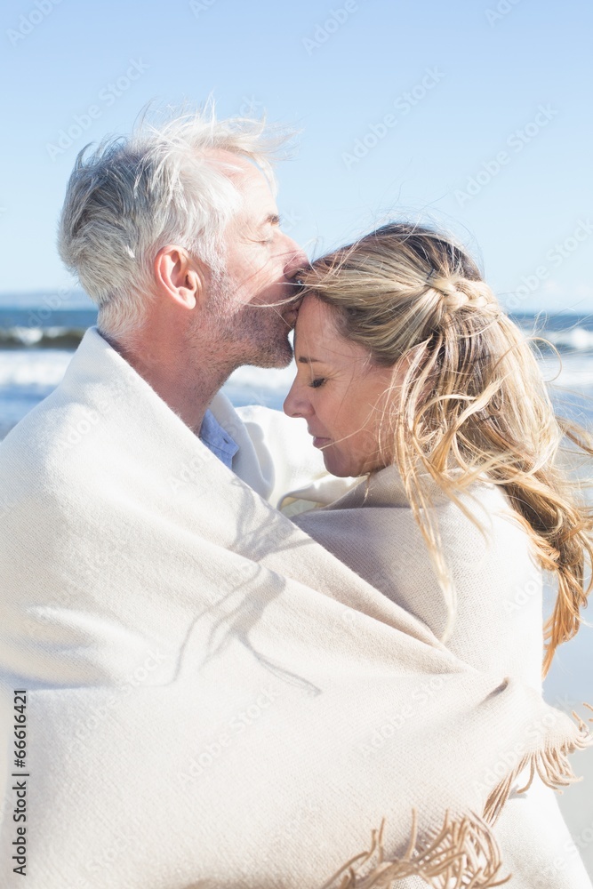 Affectionate couple wrapped up in blanket on the beach Affectionate couple wrapped up in blanket on the beach