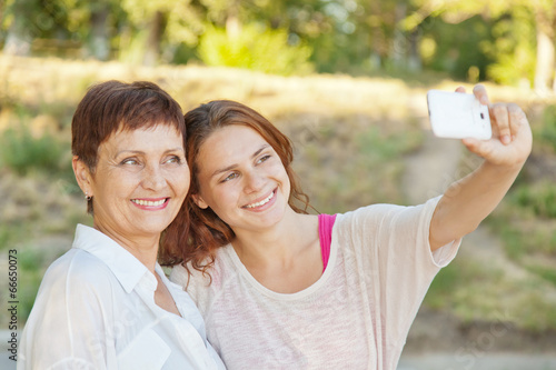mother and adult daughter are doing selfie on phone