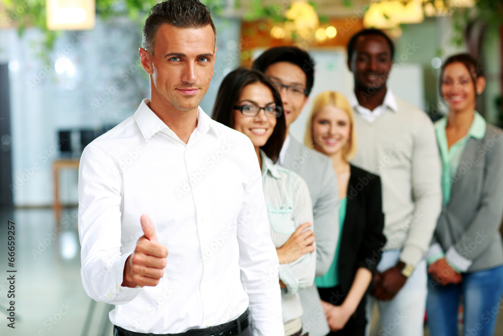 Businessman giving thumb up to camera in front of colleagues Businessman giving thumb up to camera in front of colleagues